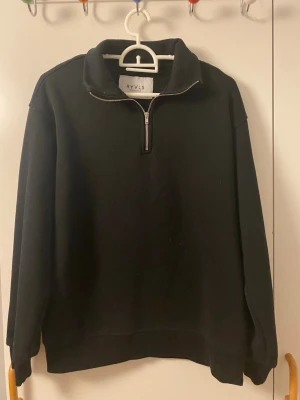 Svart halfzip sweatshirt från RYLS - Svart sweatshirt från RYLS med halv dragkedja och hög krage. Tröjan har långa ärmar, ribbade muddar och en enkel, clean design. Materialet ser ut att vara mjukt och bekvämt, troligen bomullsblandning.