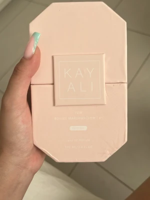 Kayali Yum Eau de Parfum Intense - Kayali Yum Eau de Parfum Intense kommer i en ljusrosa, åttakantig kartong med elegant design. Doften har noter av fresia, jordgubb, rosa marshmallow, krämig kokos, vispad vanilj och rosa mysk. Förpackningen är stilren och modern, perfekt för dig som gillar söta och fräscha parfymer.