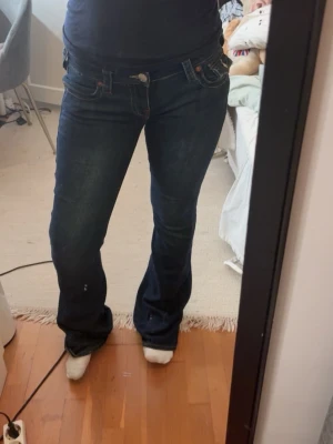 Mörkblå bootcut jeans - Säljer ett par mörkblå bootcut jeans med låg midja och klassiska fem fickor. Jeansen har kontrastsömmar och en snygg passform som sitter tajt över låren och släpper ut vid vaden. Perfekta för en avslappnad och trendig look.