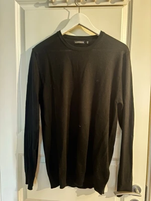 Svart stickad tröja J.Lindeberg M/S - Svart stickad tröja från J.Lindeberg med rund halsringning och diskret logga på bröstet. Tröjan har lång ärm och är tillverkad i ett tunt, mjukt material som passar perfekt till lager-på-lager-stil.