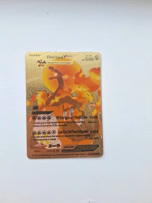Charizard VMAX Pokémonkort guld - Unikt Pokémonkort med Charizard VMAX-motiv i guld. Kortet har en glansig yta och detaljer i orange och svart, med text och effekter på engelska. Perfekt för samlare eller Pokémonfans som vill ha något extra i sin kortsamling.