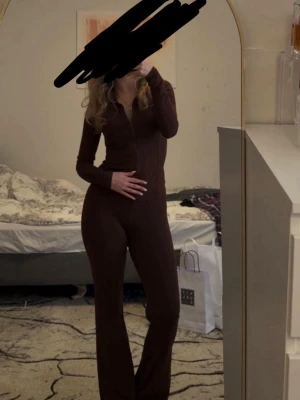 Kaffebrun träningsset  - Säljer ett snyggt set i kaffebrun färg med långärmad topp och dragkedja framtill. Byxorna är utsvängda och höga i midjan, vilket ger en trendig siluett. Materialet ser mjukt och stretchigt ut, perfekt för träning 