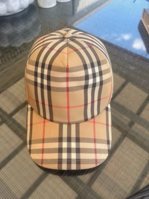 Burberry keps  - Snygg beige Burberry keps med klassiskt rutigt mönster i svart, vitt och rött. Kepsen har böjd skärm och justerbar baksida. Perfekt accessoar för att lyfta din outfit med en trendig touch. Den är äkta och är köpt på farfetch, hör av er om ni vill ha bilder!