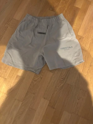 Grå shorts från Essentials Fear of God - Snygga grå shorts från Essentials Fear of God med elastisk midja och diskret logga på vänster ben. Perfekta för en avslappnad och trendig stil. Tillverkade i mjukt material för maximal komfort.