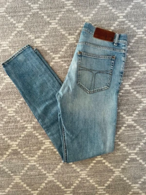 Tiger of sweden jeans  - Säljer ett par ljusblå slim fit jeans med klassisk femficksdesign och skinnpatch i midjan. Jeansen har en snygg tvättad look och raka ben. Perfekta till en avslappnad stil och passar till det mesta. Materialet är mjukt denim för skön känsla.