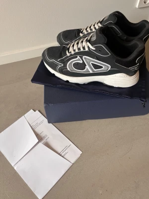 CD B30 sneakers - Säljer ett par svarta B30 sneakers med vit och grå detalj på sidan och tjock vit sula. Snygg och modern design med tydlig CD-logga på sidan. Perfekta för dig som gillar exklusiva sneakers. Se bilder för skick, fina!