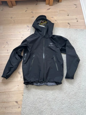 (Helt ny)Svart vindjacka från Arc'teryx  - ( KÖPT PÅ VINTED!!) ( MODDELEN ÄR 185 OCH VÄGER 75kg)Snygg svart vindjacka från Arc'teryx. Jackan har huva, hel dragkedja framtill och två snedställda fickor med dragkedja. Perfekt för dig som vill ha en lätt och funktionell jacka.