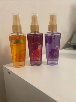 Victoria's Secret parfymmist 3-pack - Tre snygga parfymmister från Victoria's Secret: Amber Romance (orange), Pure Seduction (röd/rosa) och Love Spell (lila). Flaskorna är genomskinliga med guldfärgade spraymunstycken och blommiga detaljer. Perfekt för dig som vill ha olika dofter att välja mellan.
