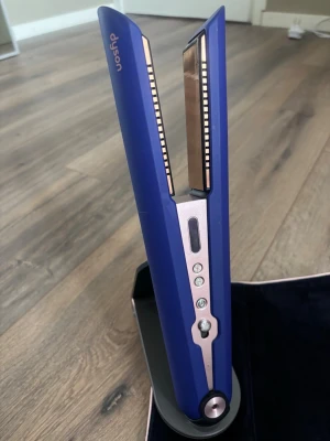 Plattång från Dyson - Dyson corrale plattång  med detaljer i roséguld. Plattången har digital display och flera knappar för temperaturinställning. Sladdlös design och laddningsstation ingår. Perfekt för att styla håret snabbt och smidigt. Fick som present men kommer inte till användning. Har endast använt 1 gång. Kommer med värmetålig väska, fällbar laddstation och laddningskabel. Plattången kan användas både med och utan kabel.  OBS! Köptes i England och kommer därför med UK kontakt, behövs reseadaptor.
