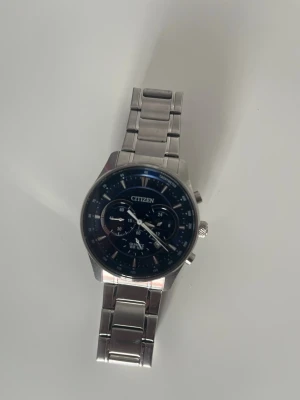 Citizen silverfärgad kronografklocka - Stilren klocka från Citizen med silverfärgad länk i metall och mörkblå urtavla. Klockan har kronograffunktion, tydliga markeringar och flera små urtavlor. Perfekt accessoar för dig som gillar klassisk och modern stil.