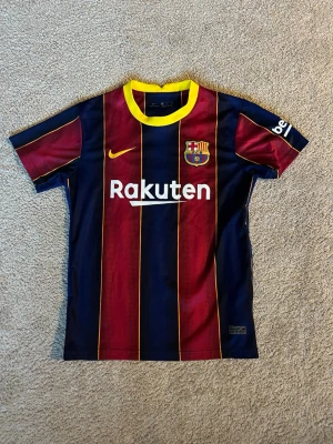 Barcelona Messi matchtröja Nike - Säljer en FC Barcelona matchtröja från Nike med Messi och nummer 10 på ryggen. Tröjan har blå och vinröda vertikala ränder, gula detaljer och klubbmärke på bröstet. Tillverkad i lätt och ventilerande material, perfekt för fotboll eller träning.