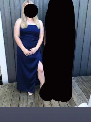 Marinblå långklänning med slits - Säljer en elegant marinblå långklänning med smala axelband och hög slits på ena sidan. Klänningen har en enkel, stilren design och är perfekt för speciella tillfällen. Materialet har en lätt glans och sitter snyggt mot kroppen.