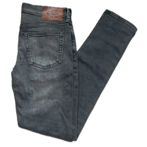 Calvin Klein jeans - Snygga svarta jeans från Calvin Klein med klassisk femficksdesign och läderpatch bak i midjan. Jeansen har raka ben och subtila slitningar för en cool look. Perfekta för dig som gillar stilrena och tidlösa plagg.