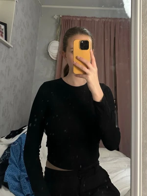 Svart croppad topp med öppen rygg - Snygg svart croppad topp med lång ärm och stor öppen rygg. Tight passform som framhäver figuren och ger en trendig look. Perfekt för dig som vill sticka ut lite extra. Materialet känns mjukt och stretchigt.