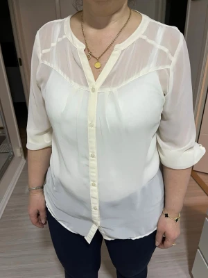 Vit transparent blus från Mexx - Stilren vit blus från Mexx i transparent material med knappar framtill och trekvartsärm. Blusen har en lös passform och fina detaljer vid axlarna. Perfekt att matcha med jeans eller kjol för en trendig look. 