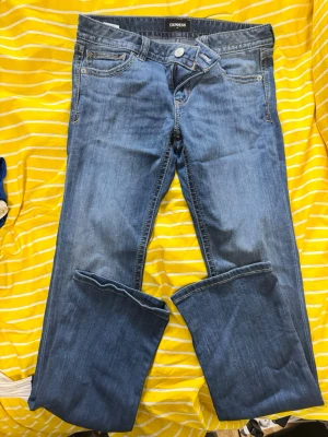 Blå bootcut jeans från Express - Säljer ett par klassiska blå bootcut jeans från Express. Jeansen har fem fickor, normal midja och är gjorda i mjukt denimtyg. Perfekta för en avslappnad och trendig look. Passar dig som gillar tidlös stil och vill ha ett par bekväma jeans i garderoben.