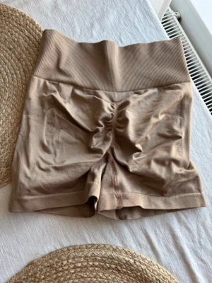 Beige seamless shorts med hög midja - Snygga beige seamless shorts med hög midja och ribbade detaljer. Shortsen har en scrunch-effekt bak och är tillverkade i ett stretchigt material som passar perfekt till träning eller chill. Inga synliga loggor eller märken. Storlek xs