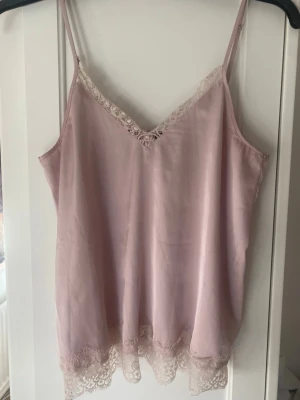 Ljusrosa linnetopp med spets H&M Divided - Säljer ett ljusrosa linnetopp från H&M Divided i storlek 34. Toppen har tunna axelband, v-ringning och fina spetsdetaljer både vid halsringningen och nertill. Materialet är mjukt och har en lätt glansig finish som ger en lyxig känsla. Använd mycket men fortfarande fin. Har katter hemma!! Förhandlar gärna om priser 