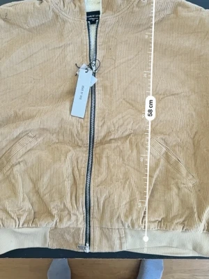 Beige fear of god bomberjacka - Snygg och stilren bomberjacka i beige manchestertyg från FEAR OF GOD. Perfekt för dig som vill sticka ut med en retroinspirerad men modern look.  Jackan har: 	•	Dragkedja framtill 	•	Två snedställda fickor 	•	Ribbade muddar vid ärmslut och nederkant 	•	Mjuk och bekväm passform  Storlek: Passar M–L men L  Perfekt både till vardags och för en mer uppklädd streetwear-stil.  💬 Hör av dig vid intresse!