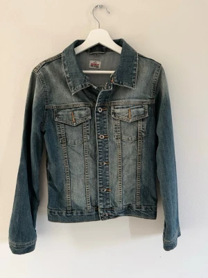 Blå jeansjacka från Colours of the World - Klassisk blå jeansjacka från Colours of the World i storlek M. Jackan har två bröstfickor med knapp, snygga sömmdetaljer och slitna kanter för en cool vintagekänsla. Passar xs och s som är i ett bra skick.