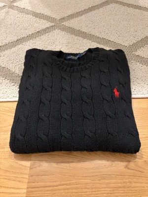 Svart Polo Ralph Lauren Cable Knit - Hej!👋  Säljer en svart cable knit sweater från Polo Ralph Lauren. Tröjan är i mycket gott skick och är sparsamt använd. Köpt second hand. Storlek: M i herrstorlek, 175/96A. Mått skickas privat!✅😀 Skickar snabbt!🚛📦 Hör av er vid frågor!💯