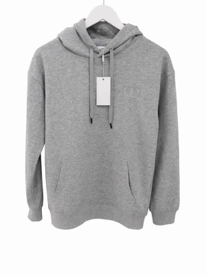 Grå hoodie från CD med broderad logga - Snygg grå hoodie från CD med broderad logga på bröstet. Klassisk modell med huva och dragsnören, samt ficka framtill. Tillverkad i mjukt bomullsmaterial som är skönt mot huden. Perfekt för en avslappnad och trendig stil. Storleken på den är L men skulle säga att den passar dig som har S-M i storlek. Hör av dig ifall du har fler frågor eller funderingar😁📦Snabb frakt, skickar samma dag📦