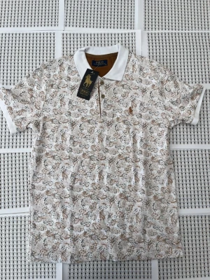 Mönstrad pikétröja från Polo Club - Snygg pikétröja från Polo Club med vit bas och detaljerat beige och brunt blommönster. Klassisk krage och korta ärmar med vita muddar. Märkets logga broderad på bröstet. Perfekt för dig som gillar stilrena men ändå unika plagg.