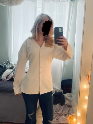 Vit blus med v-ringning och knappar - Stilren vit blus med v-ringning och knäppning framtill. Blusen har lång ärm och en rak, något lös passform. Perfekt att matcha med jeans eller kjol för en trendig look.