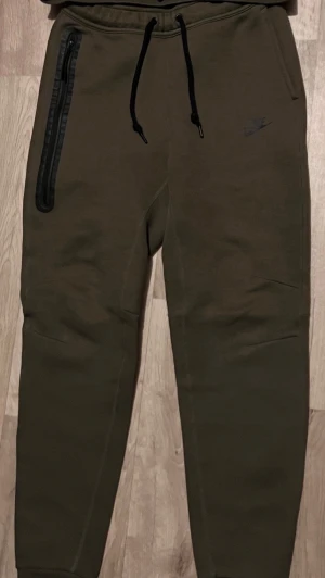 Olivgröna Nike mjukisbyxor - Säljer dessa olivgröna nike tech byxor i storlek S. Använt fåtal gånger så inga problem på den. Set med hoodie kan också köpas för 1300.