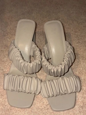 Beige sandaler med rynkade band H&M - Stilrena beige sandaler från H&M med två breda rynkade band över foten och fyrkantig tå. Tillverkade i konstläder med en trendig design som passar perfekt till sommarens outfits.