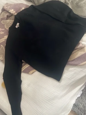 Svart stickad tröja med rund hals - En enkel svart stickad tröja med rund hals och långa ärmar. Tröjan har ribbstickade muddar vid ärmslut och nederkant, vilket ger en snygg och klassisk look. Perfekt att matcha med jeans eller kjol för en stilren outfit. Lite nopprig på vissa ställen men annars fint skick🥰
