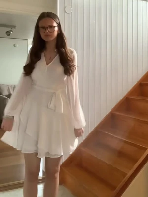 Vit skolavslutnings klänning - Snygg vit omlottklänning med v-ringning och långa, transparenta ärmar. Klänningen har ett knytband i midjan och volangdetaljer nertill. Perfekt för sommarens alla tillfällen och ger en fräsch och luftig känsla. Använt en gång förra året för min konfirmation så passar perfekt till det också! Ny pris 500kr är öppen för olika pris förslag 