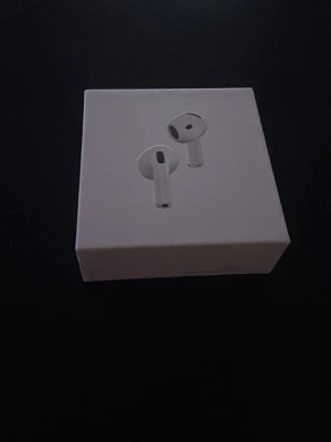 Apple AirPods med laddningsetui - Säljer ett par vita Apple AirPods med trådlöst laddningsetui och USB-C laddkabel. Hörlurarna har en stilren och minimalistisk design i blank plast och passar perfekt för dig som vill ha smidiga, trådlösa hörlurar till mobilen eller datorn.