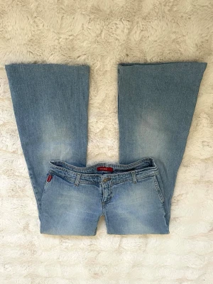 Blå bootcut jeans  - Säljer ett par ljusblå bootcut jeans med klassisk femficksdesign och låg midja. Jeansen har en lätt tvättad look och vida ben som ger en retrovibe. Perfekta för dig som gillar avslappnad stil och vill ha ett par jeans som sticker ut.