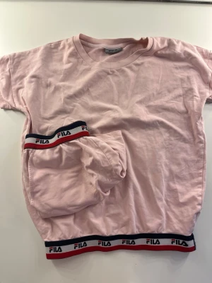 Ljusrosa pyjamas från FILA🩷 - Säljer ett ljusrosa pyjamasset från FILA med kortärmad tröja och shorts. Båda delarna har elastiska muddar med FILA-logga i rött, vitt och blått. Passar storlek s-m.