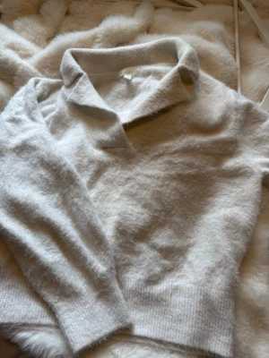 Creme vit stickad tröja med krage H&M - Mysig stickad tröja från H&M med klassisk krage och långa ärmar. Tröjan har en fluffig och mjuk känsla, perfekt för kyliga dagar. Enkel och stilren design som passar till många outfits.