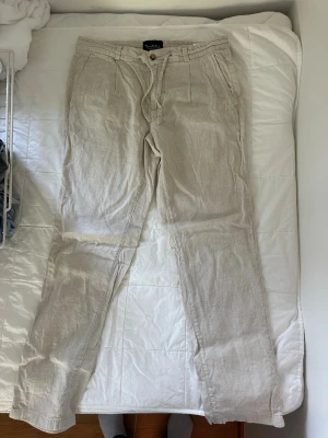 Beiga linnebyxor  - Snygga beiga linnebyxor med avslappnad passform, dragsko i midjan och knäppning fram. Byxorna har sidfickor och bakfickor med knapp. Perfekta för en chill och stilren look under varma dagar. 