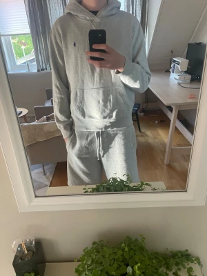 Grå hoodie från Polo Ralph Lauren - Säljer en stilren grå hoodie från Polo Ralph Lauren med liten broderad logga på bröstet. Hoodien har huva och en magficka. Tillverkad i mjukt bomullsmaterial och har ribbade muddar vid ärmslut och nederkant. Perfekt för en avslappnad look.