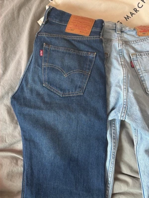 Levi's 501 mörkblå raka jeans - Klassiska Levi's 501 jeans i mörkblå denim med raka ben och femficksmodell. Jeansen har synliga kontrastsömmar, knappgylf och den ikoniska läderpatchen bak i midjan. Perfekta för en tidlös och avslappnad look.