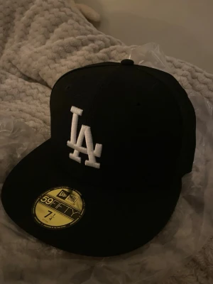 svart la new era keps - Snygg svart keps från New Era 59FIFTY med LA-logga broderad i vitt framtill och New Era-logga på sidan. Klassisk flat brim och strukturerad passform. Perfekt för dig som gillar streetwear och sportig stil. helt oanvänd