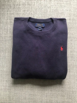 Polo Ralph Lauren tröja  - Mörkblå rundhalsad tröja från Polo Ralph Lauren med klassisk röd broderad logga på bröstet. Tröjan är stickad och har en enkel, stilren design som passar perfekt till jeans eller chinos. Kan sänka priset vid snabb affär.
