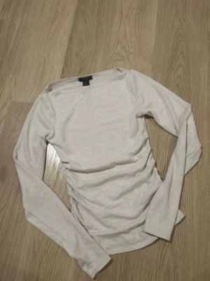 Beige långärmad topp  - En stilren beige långärmad topp. Toppen har en enkel och klassisk design med rund halsringning och är tillverkad i mjukt bomullsmaterial. Perfekt att matcha med jeans eller kjol för en clean look.