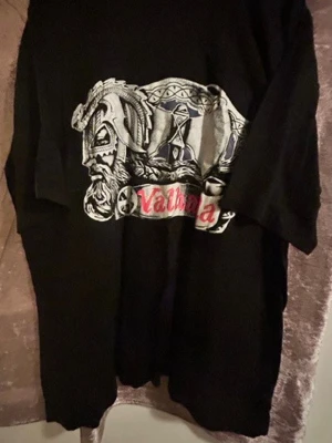 Svart Valhalla t-shirt med tryck - Cool svart t-shirt med stort Valhalla-tryck framtill. Motivet har vikingainspirerade detaljer i grått, vitt och rött. T-shirten har klassisk passform och korta ärmar, perfekt för dig som gillar unika och grafiska plagg. 100% bomull, storlek kvar L , XL och XXL 