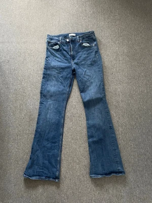 Blå bootcut jeans från Perfect Jeans - Säljer ett par blå bootcut jeans från Perfect Jeans i storlek 40. Jeansen har klassisk femficksdesign, dragkedja och knapp framtill samt lätt slitna detaljer vid fickorna. Tillverkade i denim med snygg tvättad look.