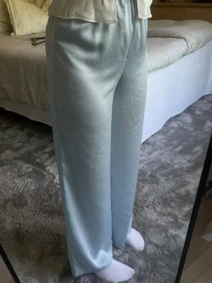Ljusblå vida satinbyxor Gina Tricot stl S - Snygga ljusblå byxor i satin med rak och vid passform. Byxorna har resår i midjan och ett mjukt, glansigt material. Använda 1 gång på temafest. Lite repiga på ena benet och två mindre fläckar i midjehöjd (syns knappt). 