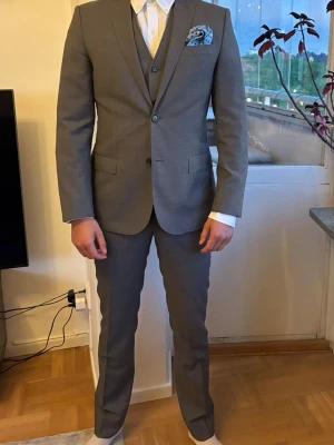 3-delad kostymset - J.Lindeberg - Stilren grå kostym med matchande väst och kavaj. Skulle säga att alla delar är ganska liten i storlek, det står 48 slim/skinny fit men jag skulle säga att det är bra mycket närmare 46.         Modell på bild är 182cm, vikt ca 75kg som vanligtvis har size 48.                                                              Använd någon enstaka gång.                             Obs. Näsduken ingår inte. 