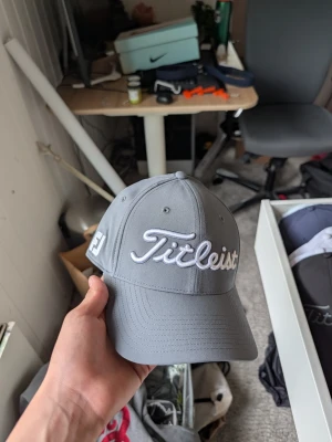 Grå Titleist keps med brodyr - Snygg grå keps från Titleist med vit broderad logga framtill och detaljer på sidorna. Klassisk böjd skärm och justerbar passform baktill. Perfekt accessoar för golf eller streetwear. Tillverkad i slitstarkt tyg med ventilerande hål.
