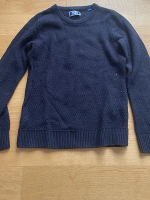 Mörkblå stickad tröja Jack & Jones - Mörkblå stickad tröja från Jack and Jones med rund halsringning och diskret strukturstickat mönster. Tröjan har långa ärmar och ribbade muddar vid ärmslut och nederkant. Perfekt för lager-på-lager och enkel att matcha. Lite nopprig och använd