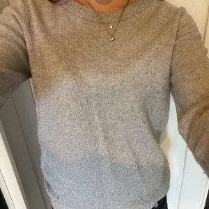 Grå stickad tröja med rund hals - Grå stickad tröja med rund halsringning och långa ärmar. Tröjan har en enkel och stilren design som passar perfekt till jeans eller kjol. Materialet ser ut att vara mjukt och bekvämt, perfekt för kyligare dagar.