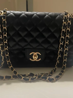 svart quiltad handväska - Klassisk svart quiltad handväska  i läder med guldfärgade kedjedetaljer och ikoniskt CC-spänne framtill. Väskan har en tidlös design med elegant kedjerem och mjukt, lyxigt material. Perfekt för dig som vill ha en ikonisk accessoar.